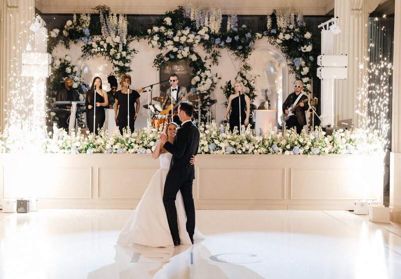 Bride and groom dancing in front of the reception band on stage with sparklers in the background