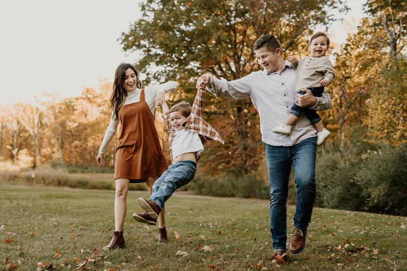 Family swinging young son in fall