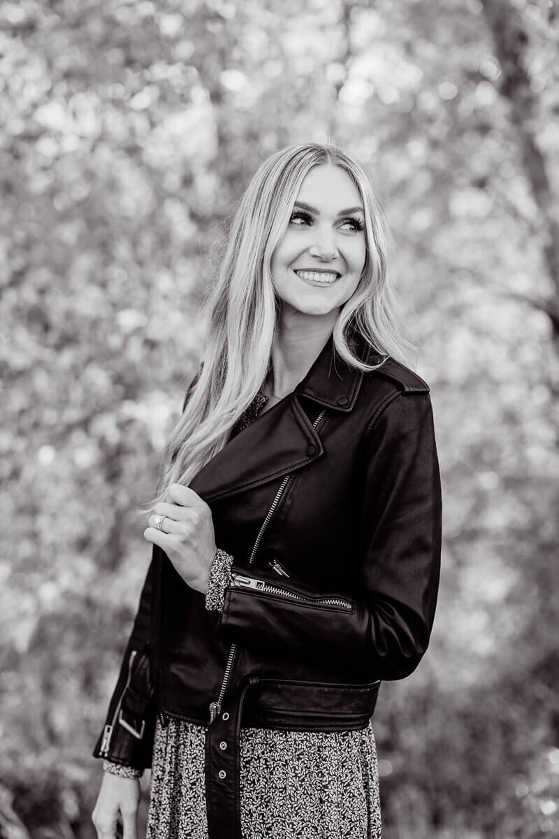 blonde woman in black  leather jacket smiling and looking away from camera
