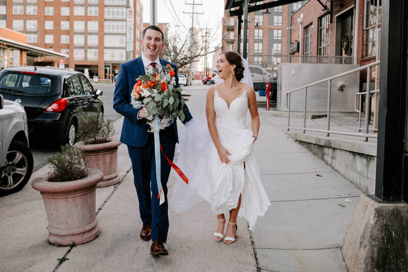 bride and groom walking down sidewalk while smiling