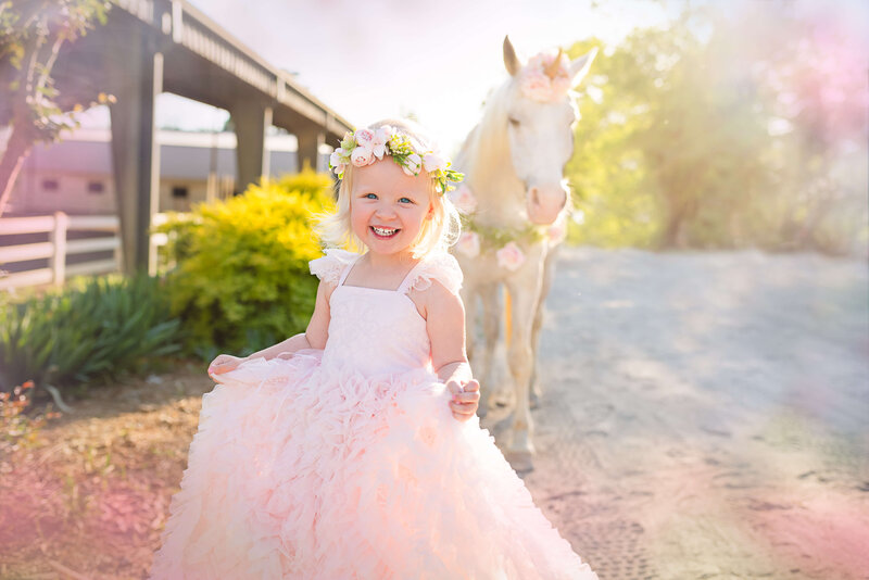 Girl wearing a pink fancy dress smiling with a unicorn