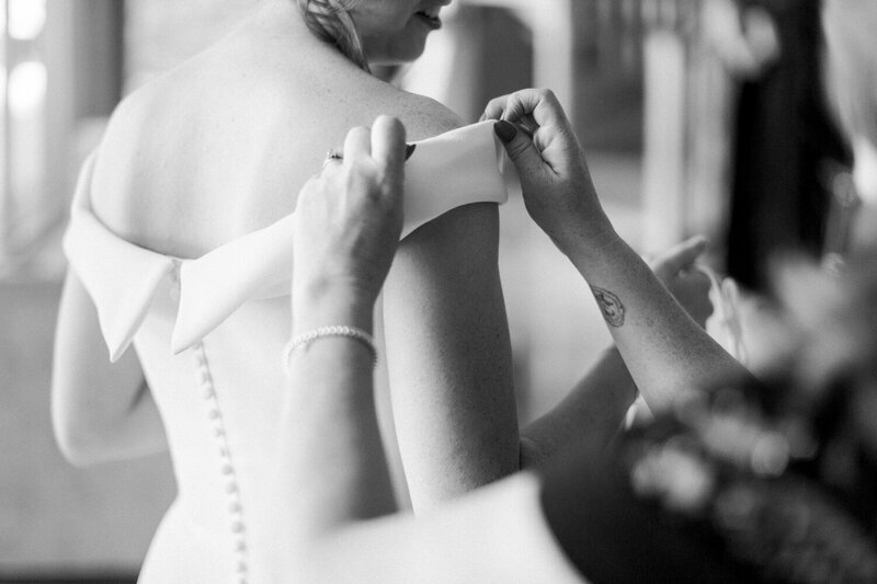 This poignant image captures the bride and her mother sharing a tender moment as they prepare for the wedding. The mother assists with the bride's dress, symbolizing both support and love on this significant day.
