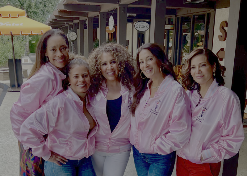 Latinas Acting Up founders and board members Gina Torres, Lisa Vidal, Diana Maria Riva, Angelique Cabral, and Constance Marie wearing matching pink LAU jackets at an outdoor event