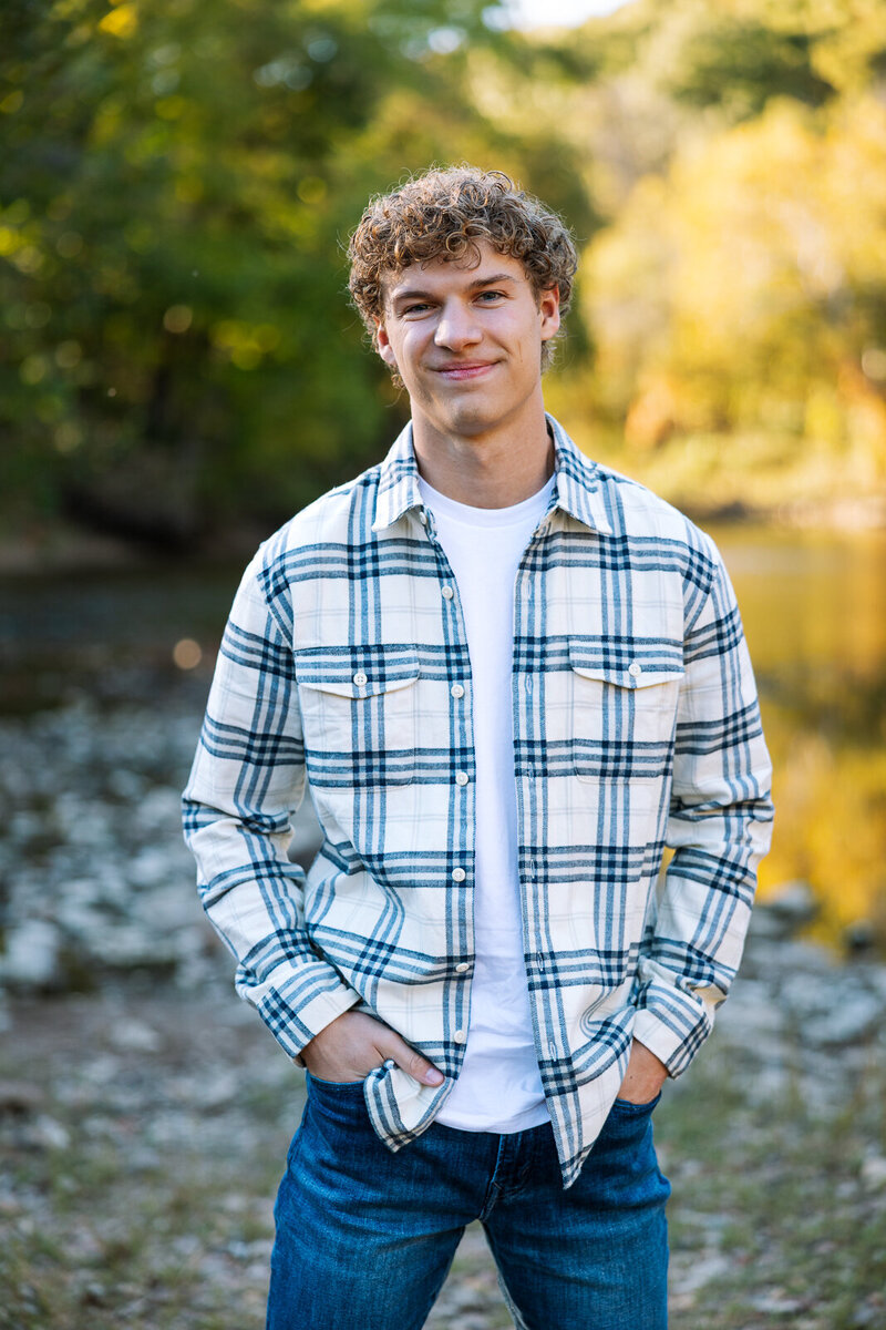 Senior guy standing with hands in pocket smiling at camera while at the river. 