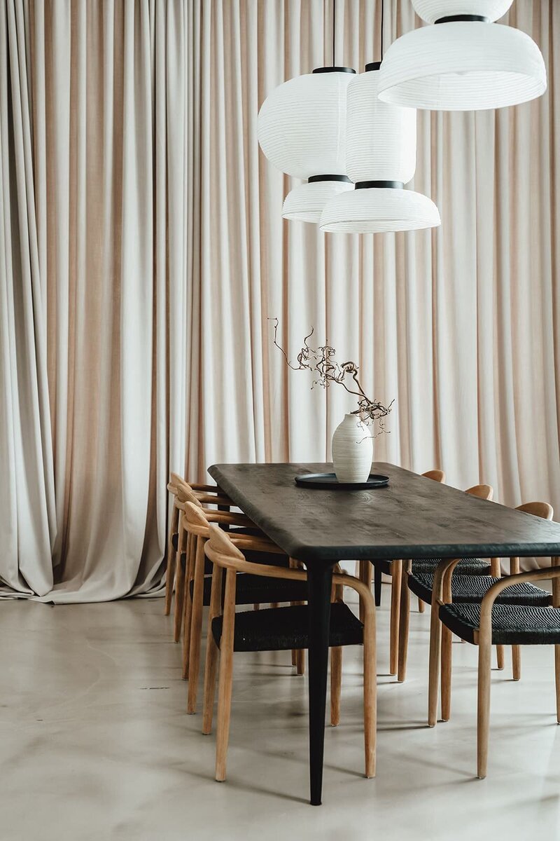 Studioaufnahme: Licht durch die Sprossenfenster erzeugt ein faszinierendes Schattenspiel auf dem Boden. Im Vordergrund sind die Designer-Schaukel und die Pfeiler des Studios zu sehen, während im Hintergrund ein wallender Vorhang, eine Backsteinwand und ein Fenster die Szene vervollständigen
