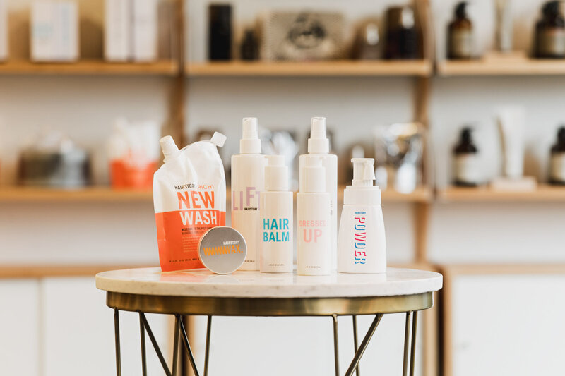 A collection of Hairstory hair products displayed on a round table representing non-toxic hair products used at the The Collective Beauty and Wellness.