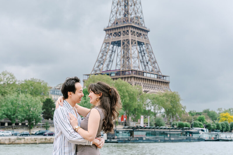 miling couple embracing in front of the Eiffel Tower at Passerelle Debilly near Palais de Tokyo during a romantic Paris proposal photoshoot.