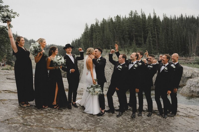 Wedding party cheer while couple kisses at Elbow Falls near Calgary Alberta