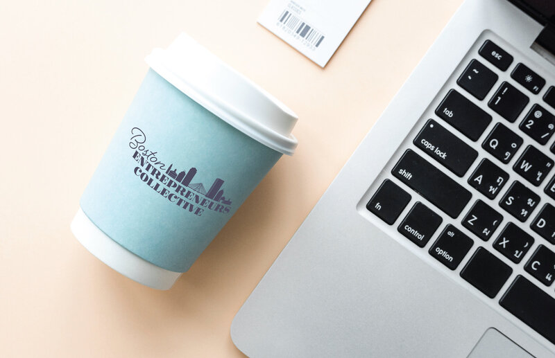 Image of disposable coffee mug with logo printed on sleeve displayed next to laptop.