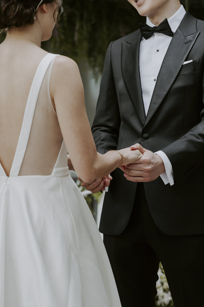 a bride wearing a white wedding dress and a groom wearing a balck tuxedo hold hands during their ceremony in seoul