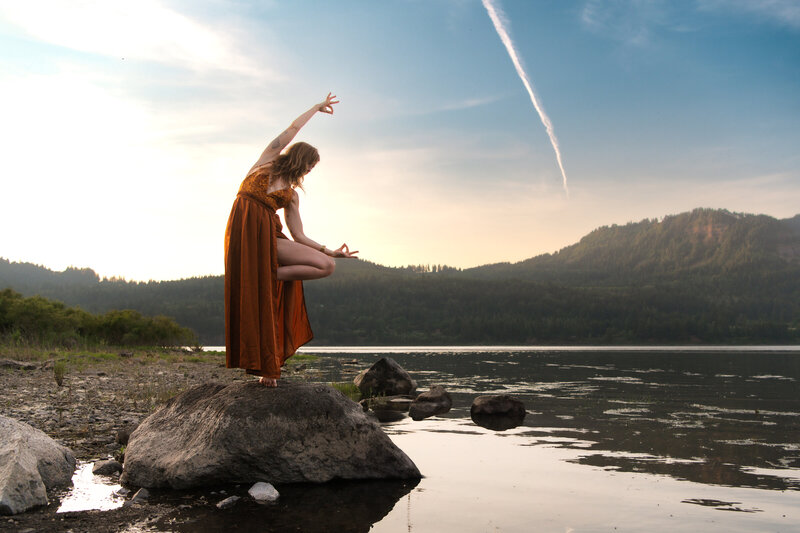woman doing a yoga pose on river rocks