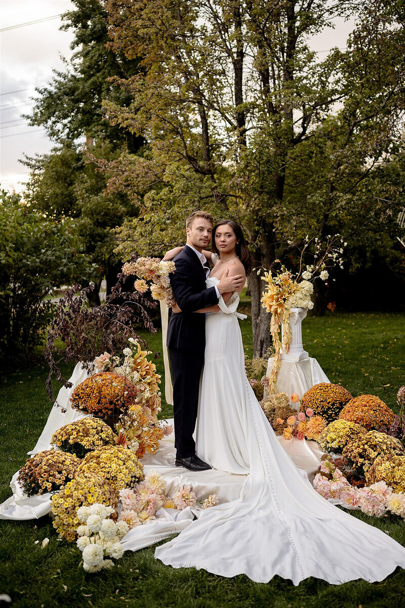bride and groom pose with elaborate floral arrangements in utah