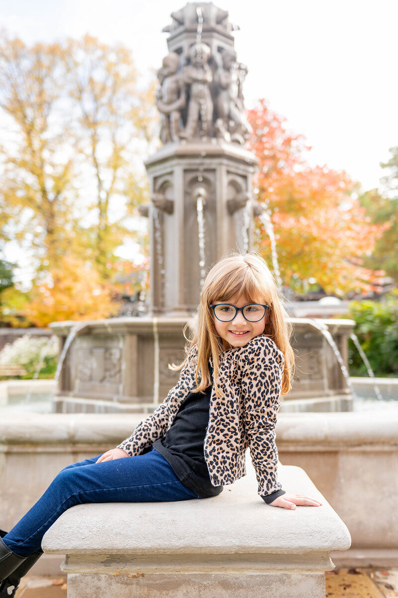 A young girl with long hair and glasses, wearing a leopard print cardigan and jeans, leaning back and smiling - Bloom by bel monili