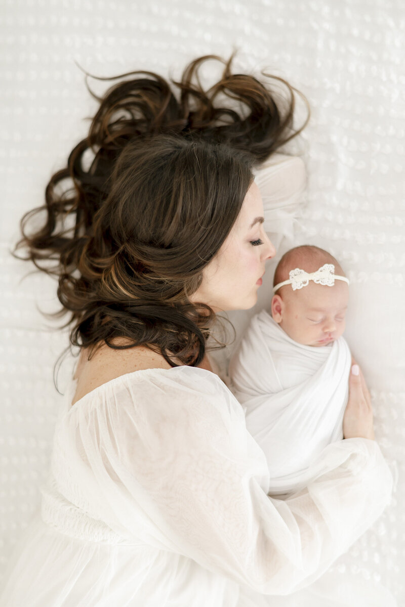 A mother lays with her hair spread out and arm around her Nashville newborn