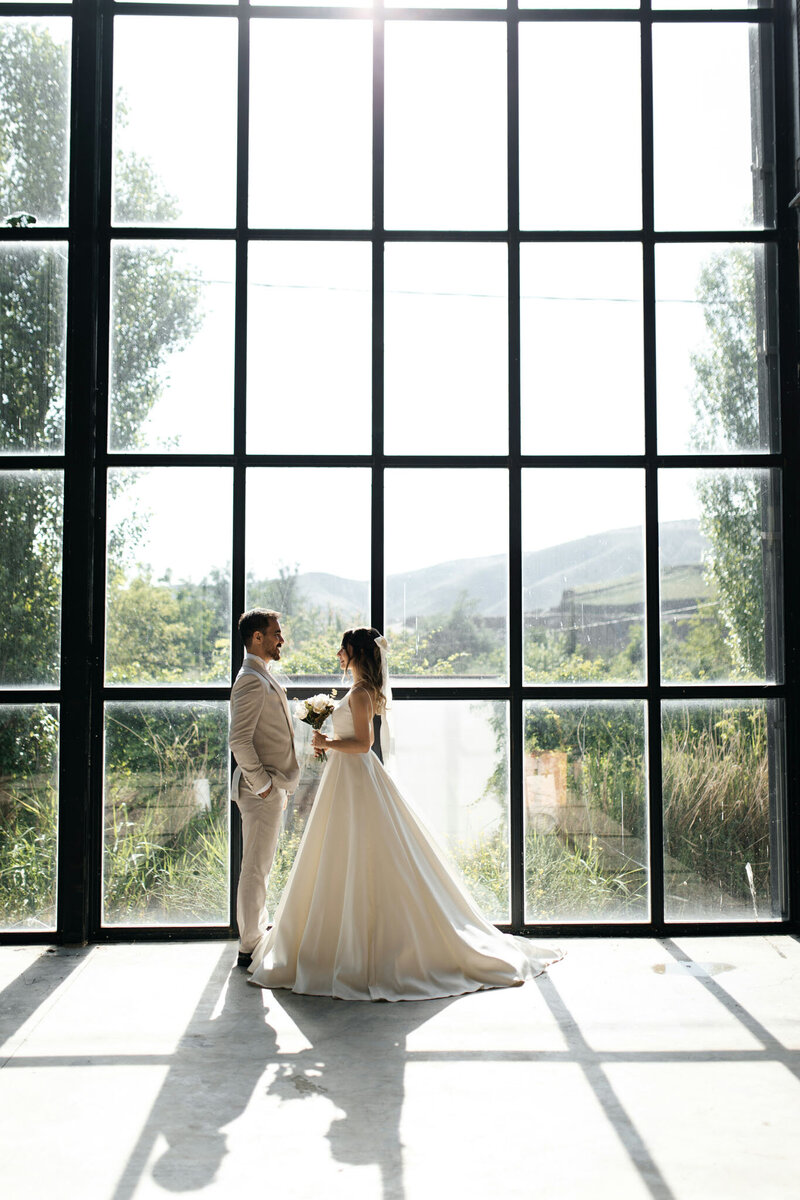 Bride and groom standing in front of a large glass window with scenic view