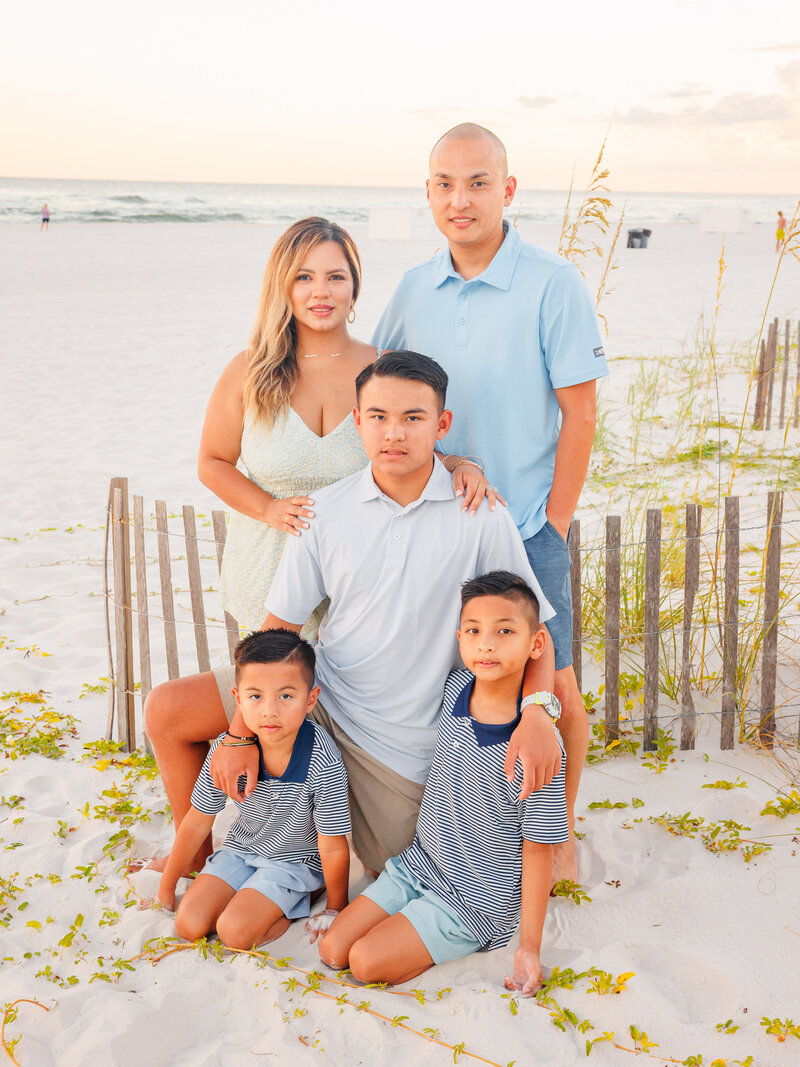 Family of 5 with 3 boys kneeling in front of water during golden hour