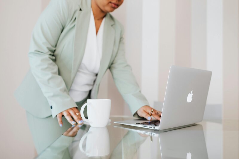 woman in mint green suite standing at desk typing on laptop