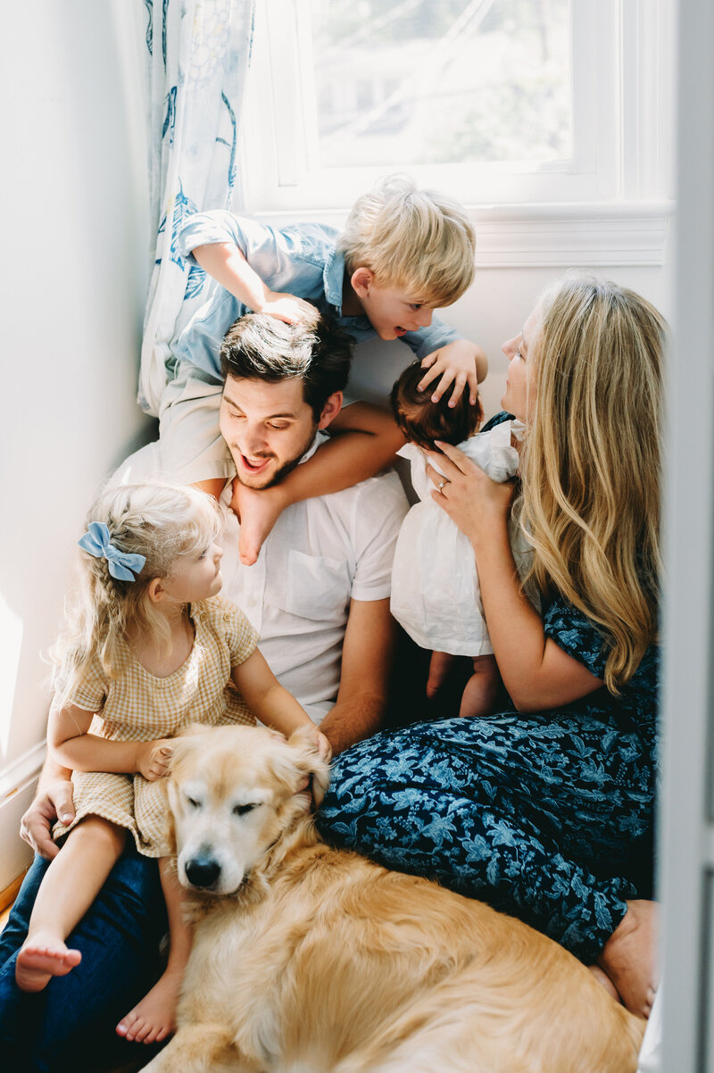 family of five with golden retriever playing under a window