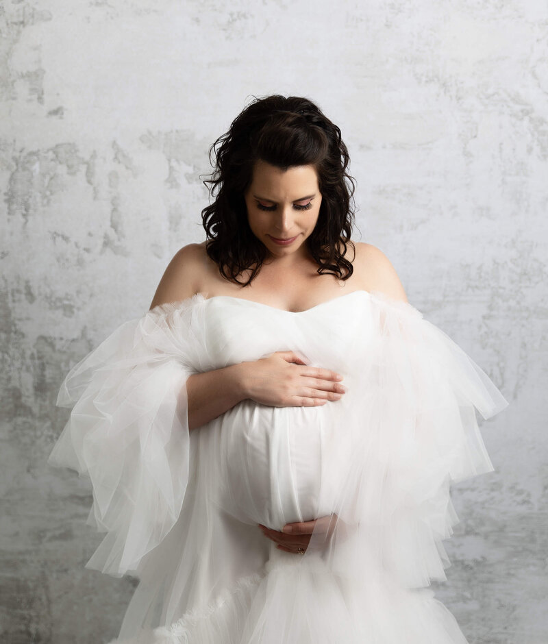 Photo of a young mother posing for maternity portraits in a white dress in an Erie Pa photography studio