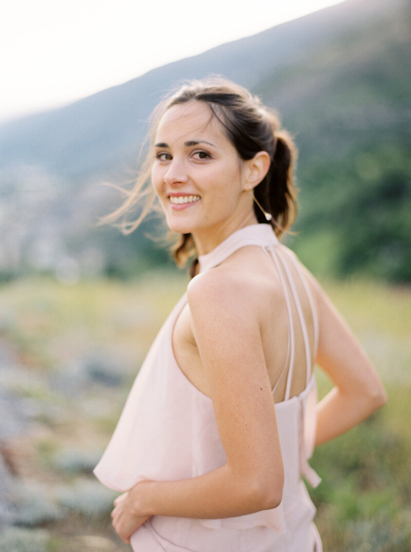 Woman in pink chiffon dress smiles while looking back over her shoulder