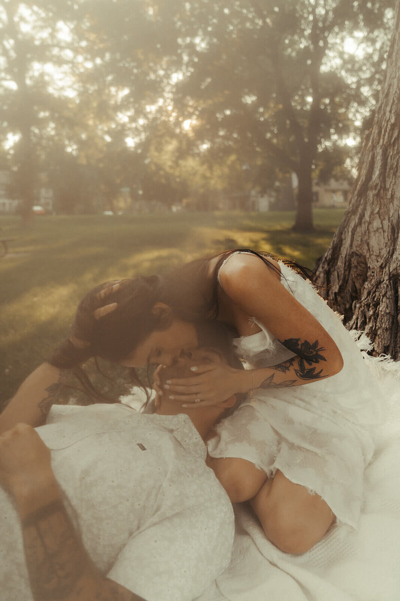 Woman leans down to kiss her fiance with his head in her lap