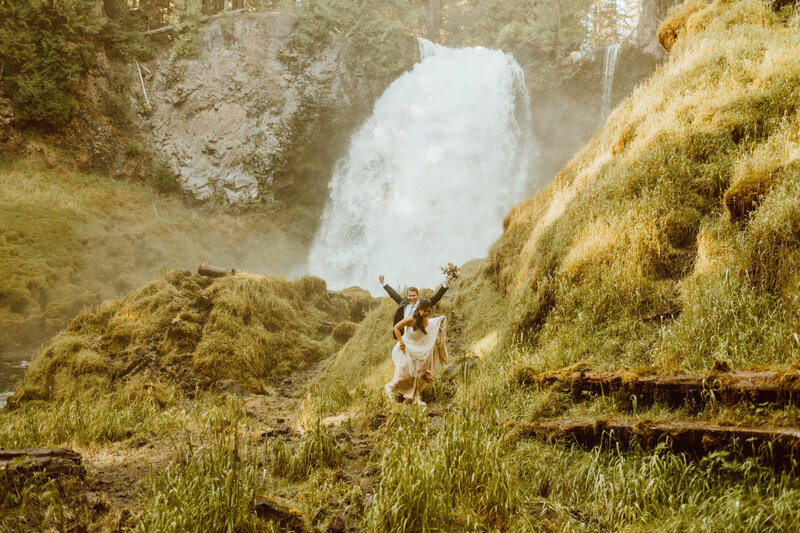 bride and groom walking in front of a waterfall