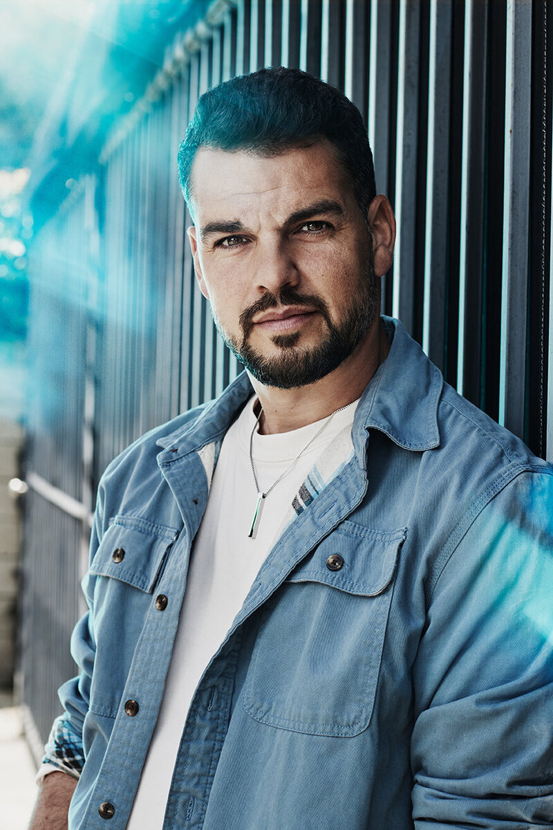 Outdoor portrait of David Victori in a denim jacket and white shirt, leaning against a textured wall, photographed by Ylva Erevall.