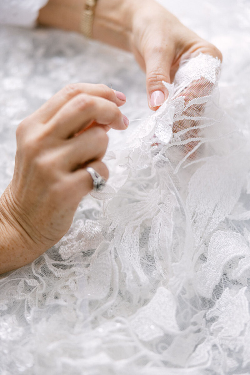 Bridal seamstress hand-stitching delicate lace fabric for a custom wedding gown