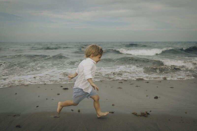 little boy runs along beach during family photos
