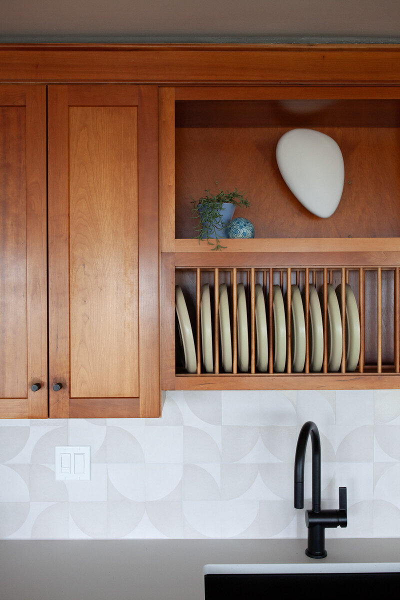 Kitchen details of an Oregon beach house rental featuring a wooden cabinet with open slots for dishes, a black sink fixture and a patterned wall backsplash.