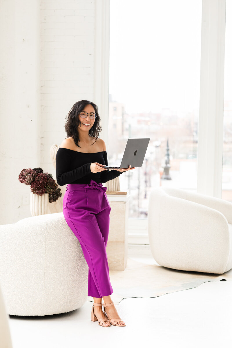 Anh Nguyen, NYC graduation photographer, smiling while editing photos on a laptop.