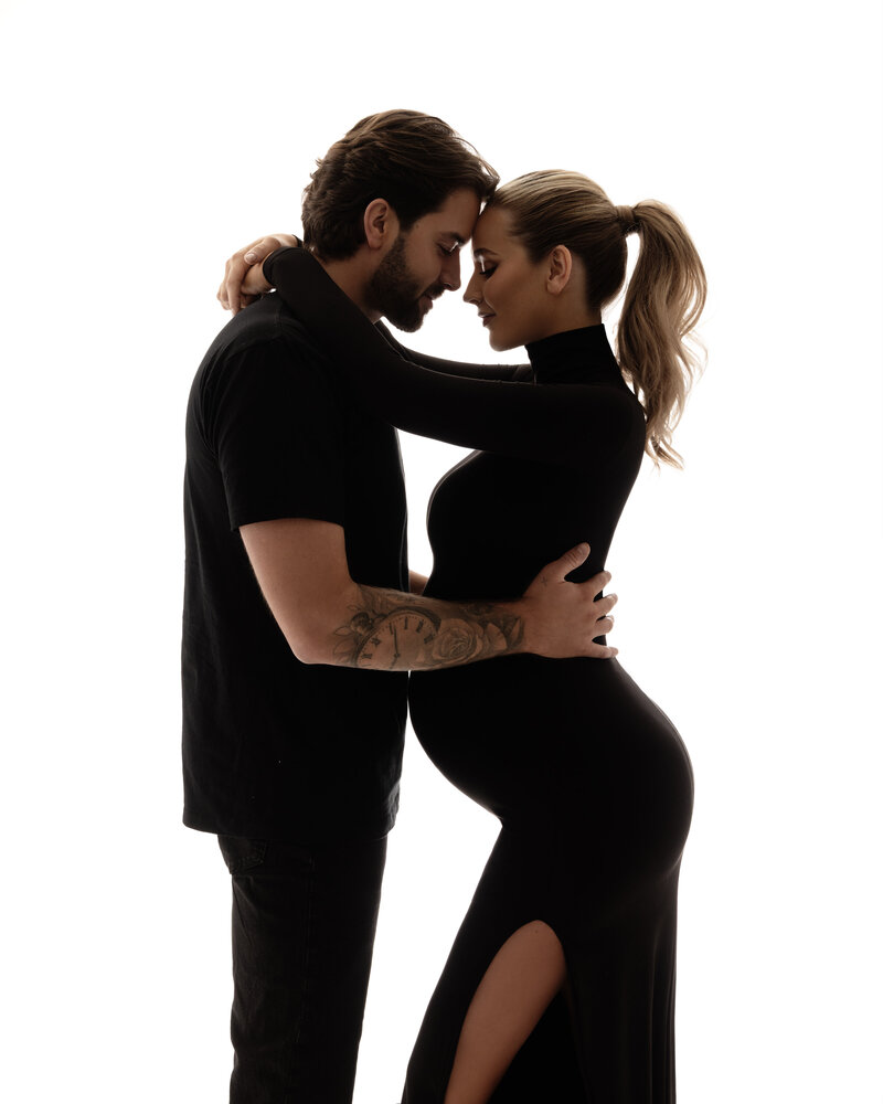 An expectant mother and her partner sharing a tender embrace, both smiling and looking towards the future.