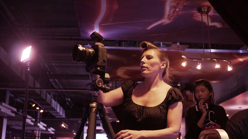 Ylva Erevall directing a photoshoot at a bowling alley, focused behind the camera amidst vibrant, cinematic lighting.