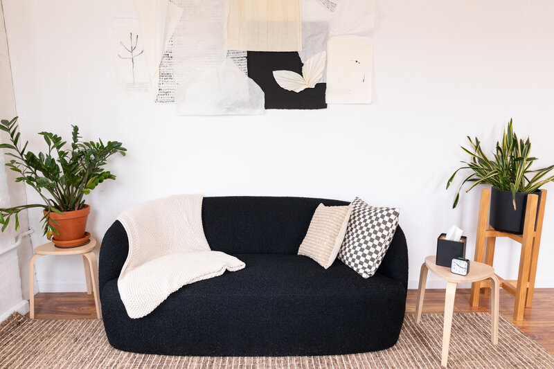 Black couch with throw pillows and blanket atop and a piece of collaged artwork hung above it.