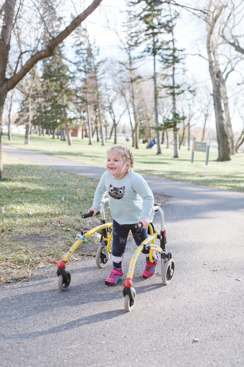 A child walking in the park supported by a gait trainer.