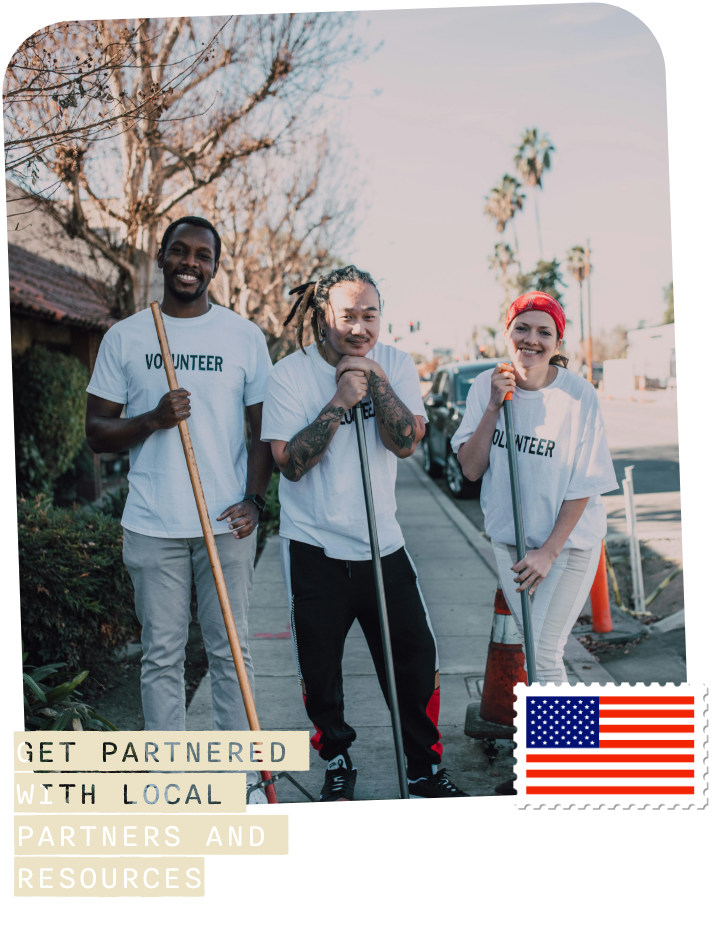 three individuals wearing a white volunteer shirt and each holding rakes