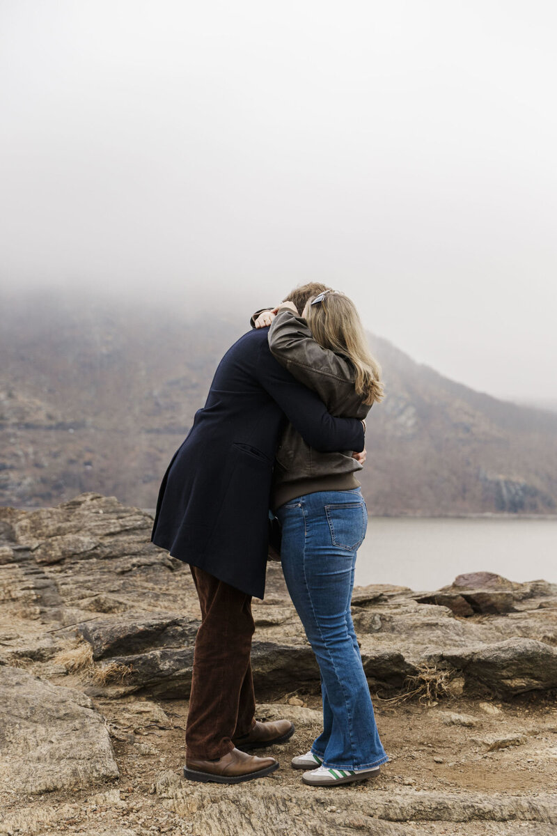 Newly engaged couple hugging on a misty Hudson Valley overlook after a surprise proposal