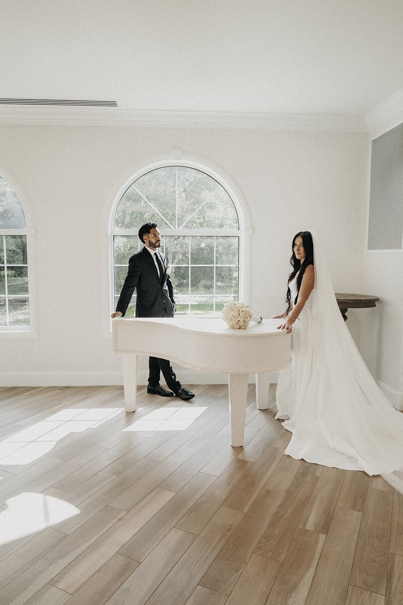 wedding couple at white piano by large window flowing wedding dress