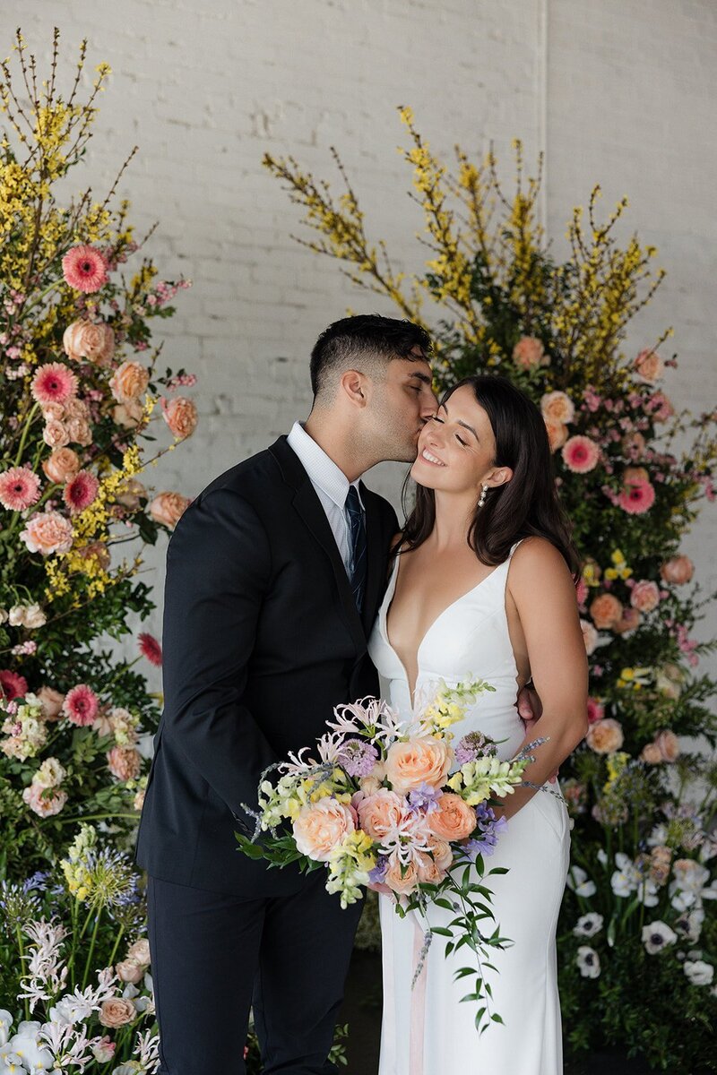 Couple kissing in front of floral set up designed by Helena Elizabeth Events, wedding planner brooklyn