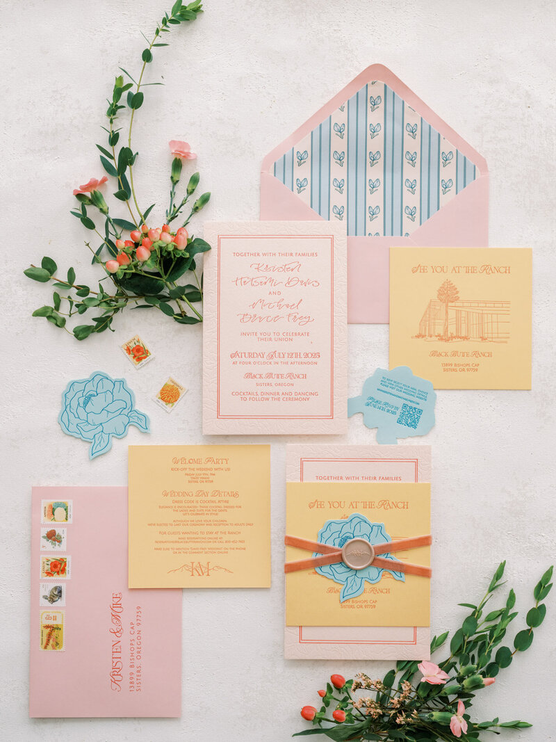 Customized calligraphy flat lay featuring wedding invitations, envelopes, flowers and more represent full service design by Life in Letters.