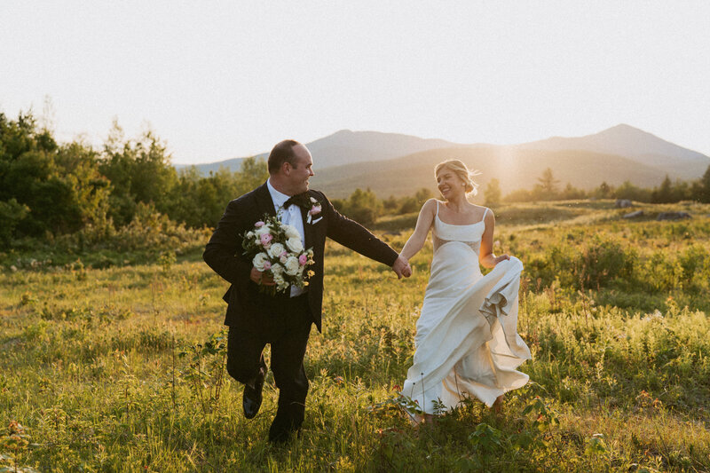Bride and groom running hand in hand through a field in Chocorua, New Hampshire at sunset.