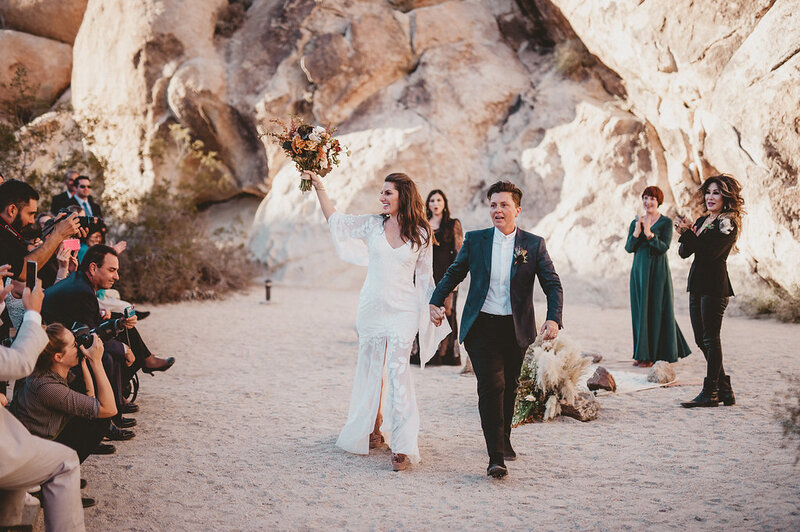 A lesbian couple's desert wedding ceremony exit towards the camera.