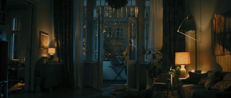 A character framed by window light, lost in thought, evoking emotional complexity.