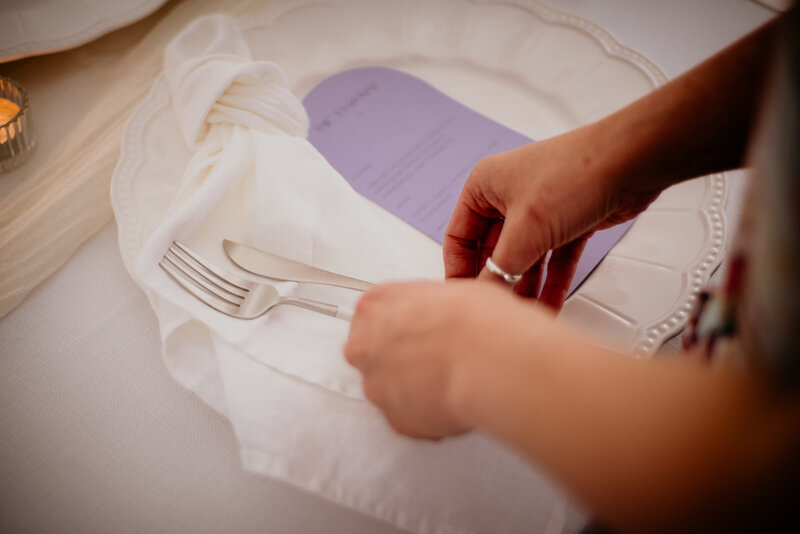 Lilac purple wedding menu with arched design and guest name at the top, next to hands holding white cutlery