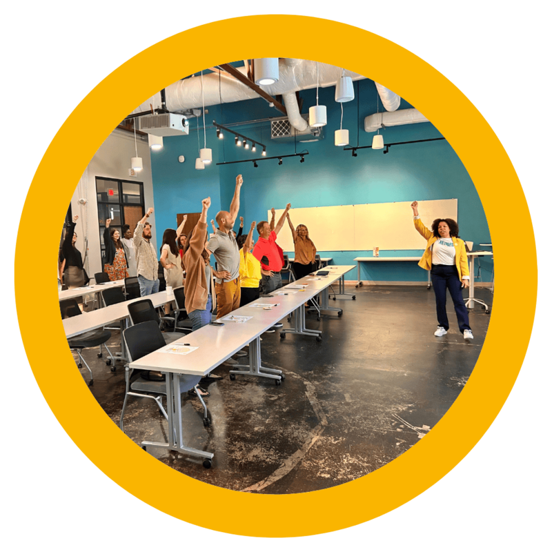 Photo of Michelle McKown-Campbell leading an employee workshop. Everyone has their hands up in celebration. 