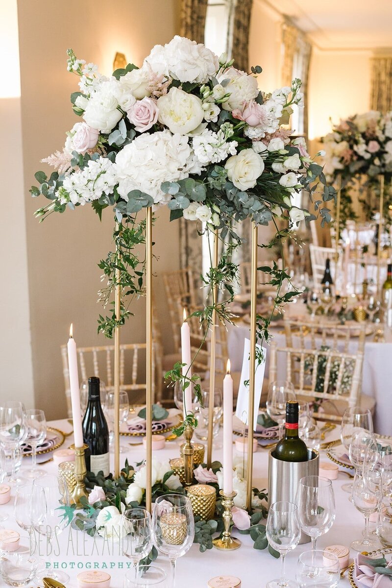 A tall gold stand of flowers on a table for this Cornwall wedding