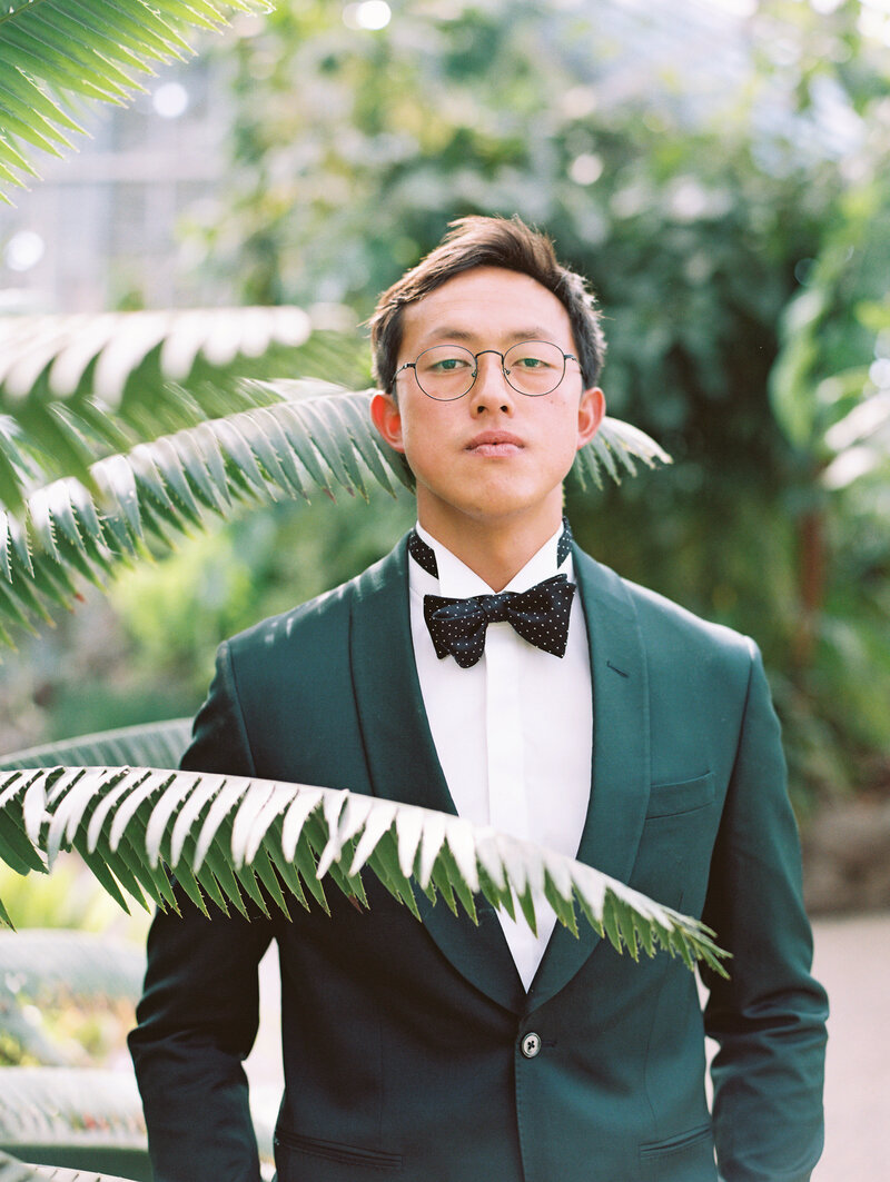 A portrait of the handsome and fashionable groom, who looks towards the camera for his close-up, by photographer Megan Lynn of My Sun and Stars Co. at the tropical venue Dos Pueblos Orchid Farm.