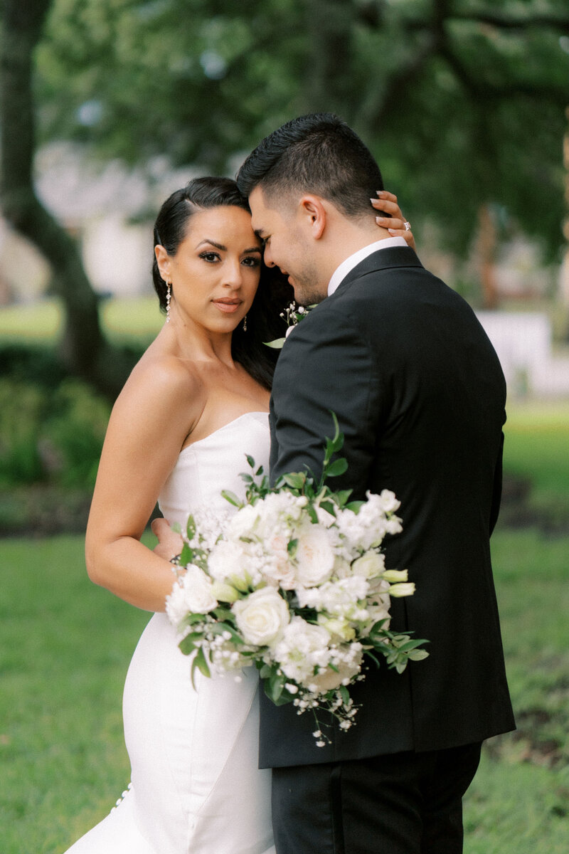 Bride and groom with their arms interlocked smiling at each other in front of a brick wall
