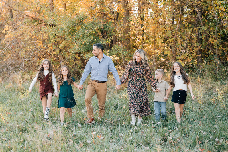 A family of six walking hand in hand through a golden autumn field.