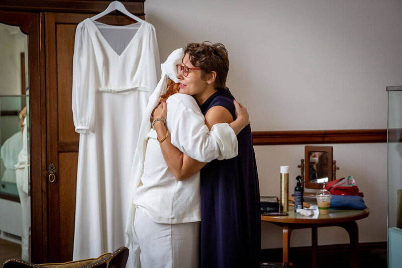 Bride in white pyjamas and wearing white bow in hair hugging friend in Town Hall Hotel ready for her London wedding